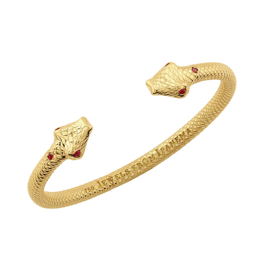 An 18K yellow gold ring with two snake head adornments and round-cut ruby eyes, with the phrase 'JEWELS FROM IPANEMA' inscribed on the surface.